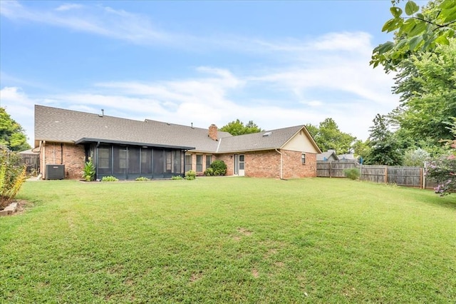 rear view of house with central AC, a sunroom, and a lawn