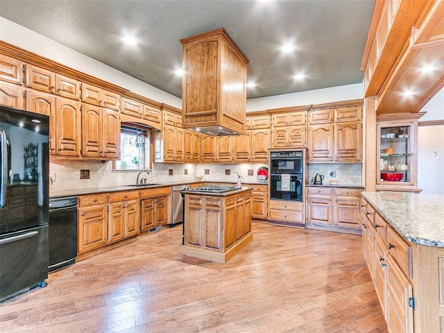 kitchen featuring light hardwood / wood-style flooring, tasteful backsplash, black appliances, a kitchen island, and sink