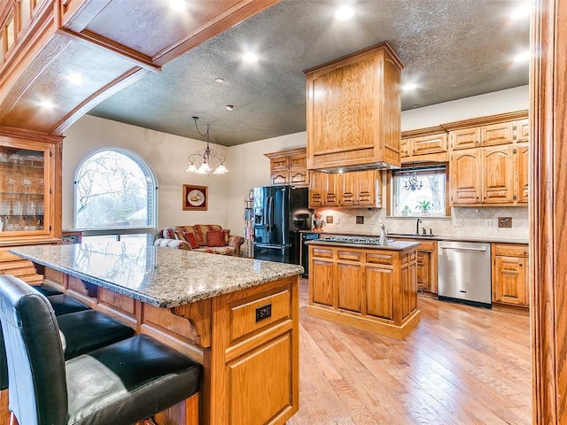 kitchen featuring light hardwood / wood-style flooring, a kitchen island, black refrigerator with ice dispenser, dishwasher, and a kitchen breakfast bar