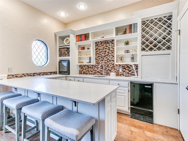 kitchen featuring light hardwood / wood-style flooring, a breakfast bar, sink, white cabinetry, and kitchen peninsula