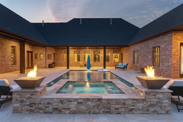 pool at dusk featuring an in ground hot tub, a patio area, and a fire pit