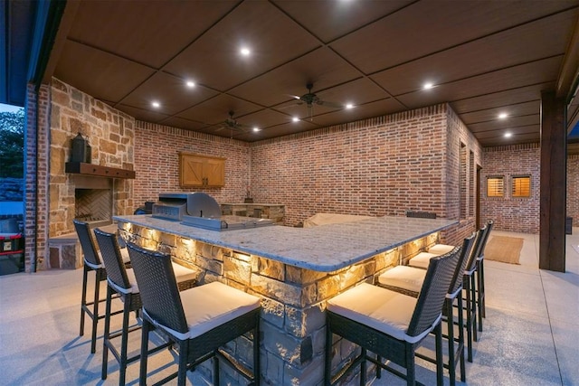 bar featuring light stone countertops, brick wall, a drop ceiling, and ceiling fan