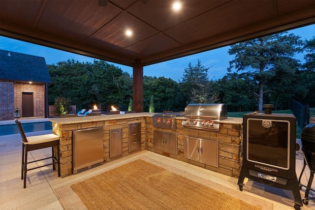 patio terrace at dusk with an outdoor kitchen and area for grilling