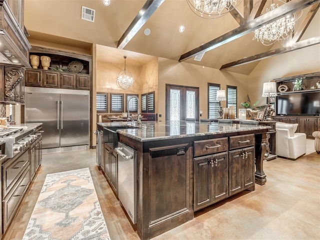 kitchen featuring an inviting chandelier, hanging light fixtures, dark brown cabinets, a center island with sink, and built in fridge