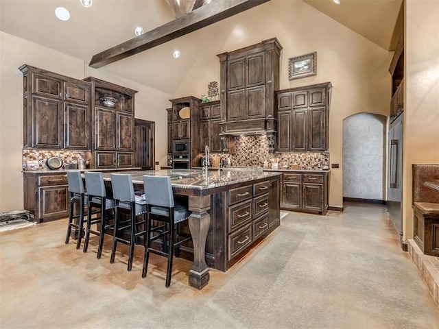 kitchen with a breakfast bar area, high vaulted ceiling, dark brown cabinetry, a center island with sink, and decorative backsplash