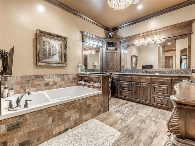 bathroom featuring wood-type flooring, ornamental molding, vanity, tiled tub, and an inviting chandelier