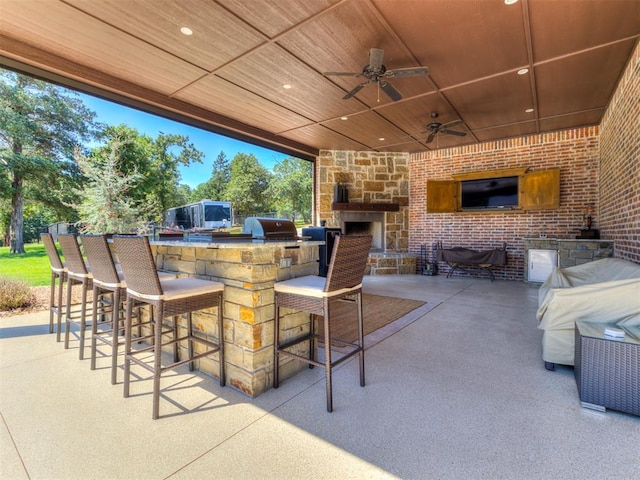 view of patio with exterior bar, a grill, an outdoor kitchen, an outdoor stone fireplace, and ceiling fan