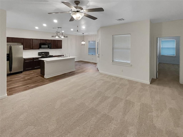 kitchen with pendant lighting, carpet floors, black appliances, dark brown cabinets, and a center island with sink