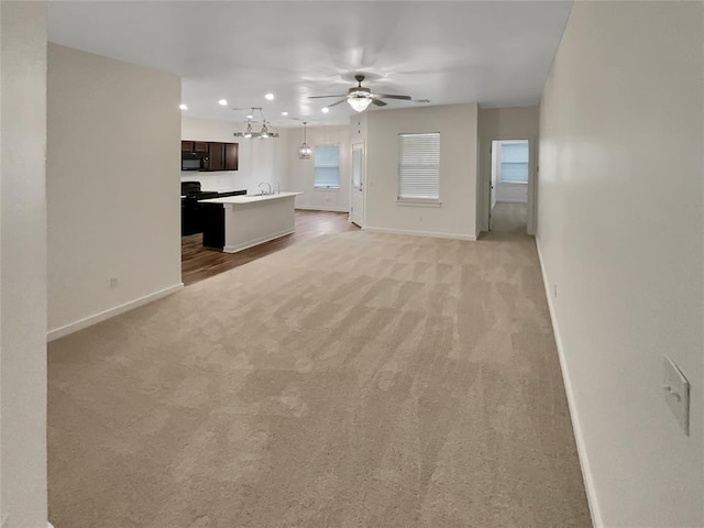 unfurnished living room featuring sink, light colored carpet, and ceiling fan