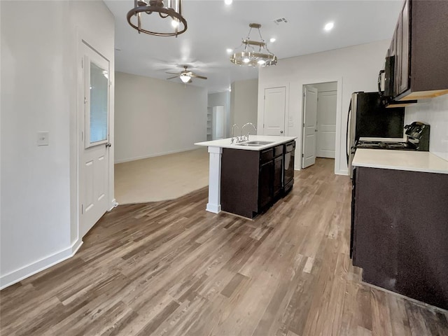 kitchen featuring pendant lighting, sink, ceiling fan, a kitchen island with sink, and stove