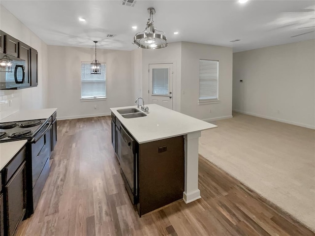 kitchen featuring decorative light fixtures, sink, black appliances, a center island with sink, and light wood-type flooring