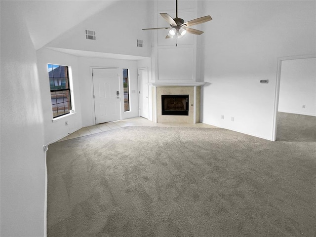 unfurnished living room with a tiled fireplace, high vaulted ceiling, light colored carpet, and ceiling fan