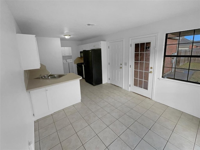 kitchen featuring black refrigerator, white cabinetry, sink, stove, and washing machine and dryer