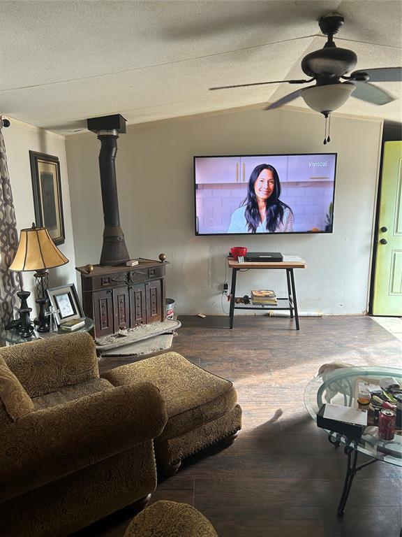 living room featuring hardwood / wood-style floors, lofted ceiling, a wood stove, ceiling fan, and a textured ceiling