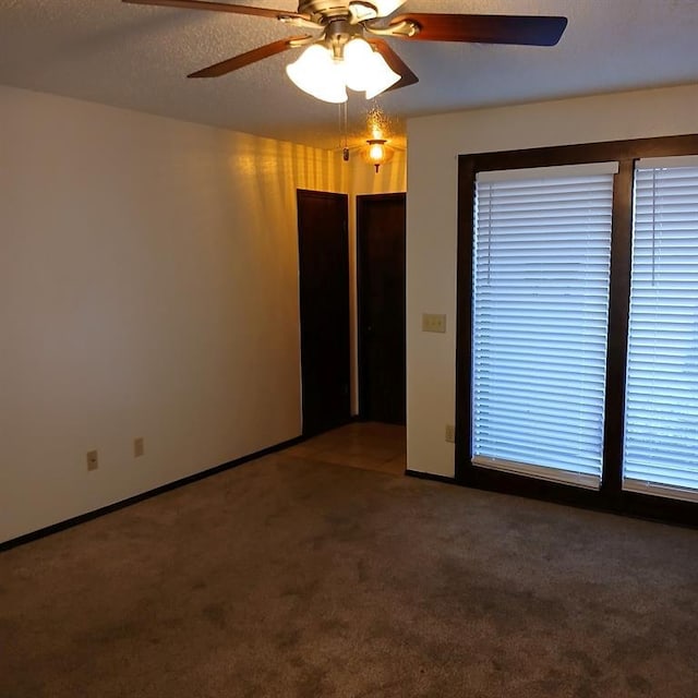 empty room featuring ceiling fan, a textured ceiling, and dark colored carpet