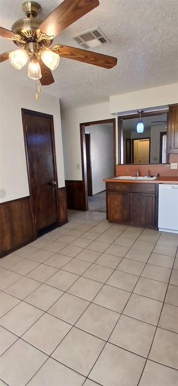 kitchen with sink, dishwasher, wooden walls, a textured ceiling, and light tile patterned flooring