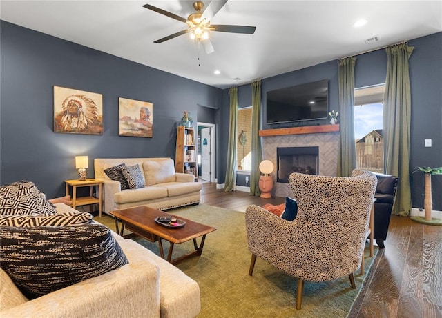 living area with wood finished floors, a fireplace, a ceiling fan, and visible vents