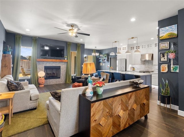 living room featuring a tiled fireplace, ceiling fan, recessed lighting, and dark wood finished floors