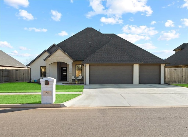 french provincial home with stone siding, a garage, fence, a front lawn, and driveway