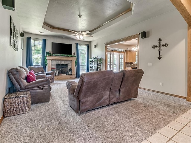 living room featuring a tiled fireplace, ceiling fan, a raised ceiling, and light tile patterned floors