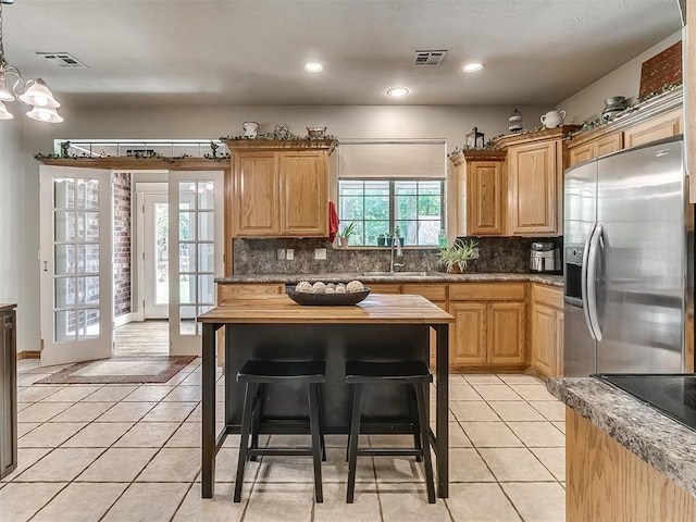 kitchen featuring stainless steel refrigerator with ice dispenser, light tile patterned flooring, french doors, sink, and decorative light fixtures