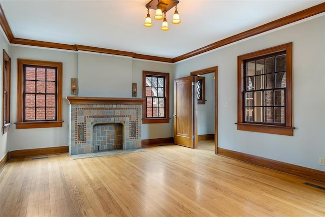 unfurnished living room featuring a tiled fireplace, ornamental molding, a chandelier, and light wood-type flooring