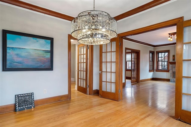 unfurnished dining area with an inviting chandelier, crown molding, french doors, and light wood-type flooring