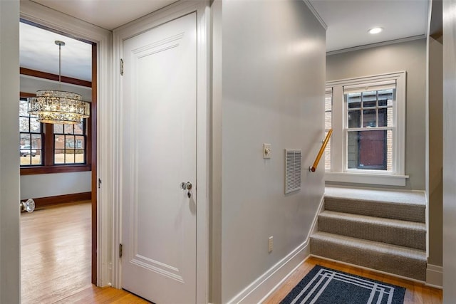 stairway with hardwood / wood-style flooring, crown molding, and an inviting chandelier