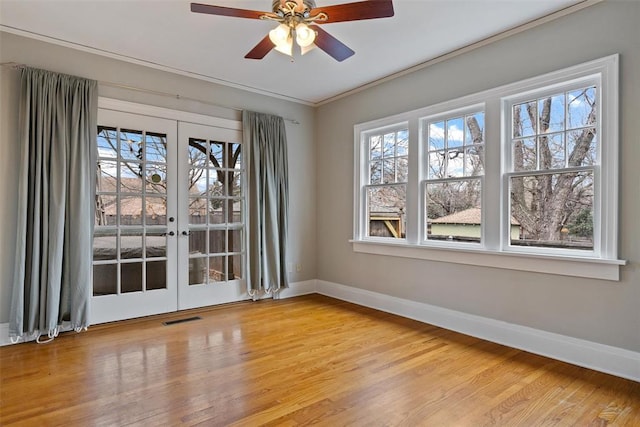 empty room with crown molding, plenty of natural light, hardwood / wood-style floors, and french doors