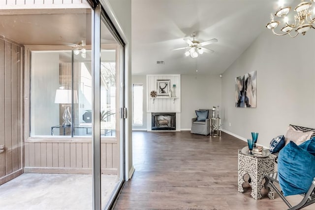 interior space with vaulted ceiling, dark wood-type flooring, ceiling fan with notable chandelier, and a fireplace