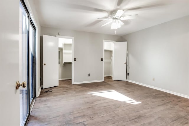 unfurnished bedroom with hardwood / wood-style flooring, a walk in closet, a closet, and ceiling fan