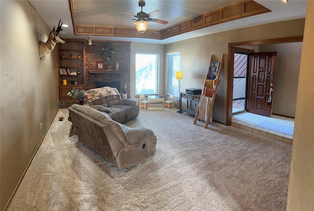 carpeted living room with a brick fireplace, a raised ceiling, and ceiling fan