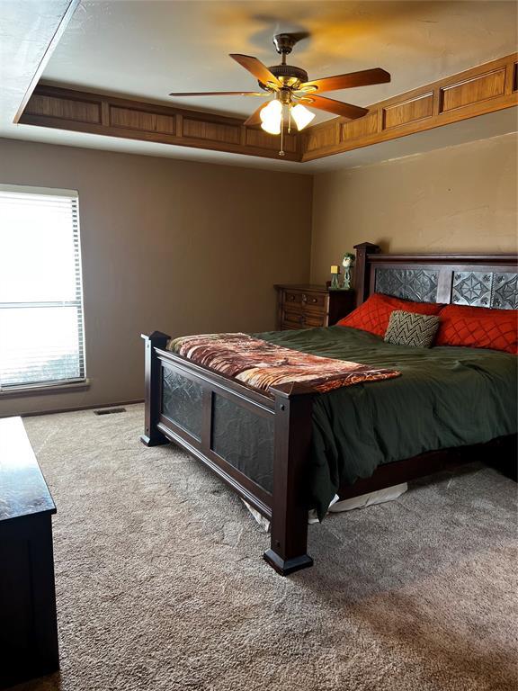 carpeted bedroom featuring ceiling fan and a tray ceiling