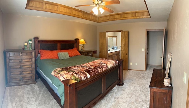 bedroom with ensuite bath, light colored carpet, a raised ceiling, and ceiling fan