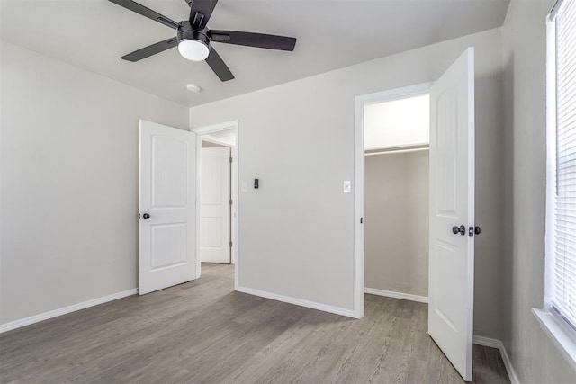 unfurnished bedroom with ceiling fan, a spacious closet, light hardwood / wood-style floors, and a closet