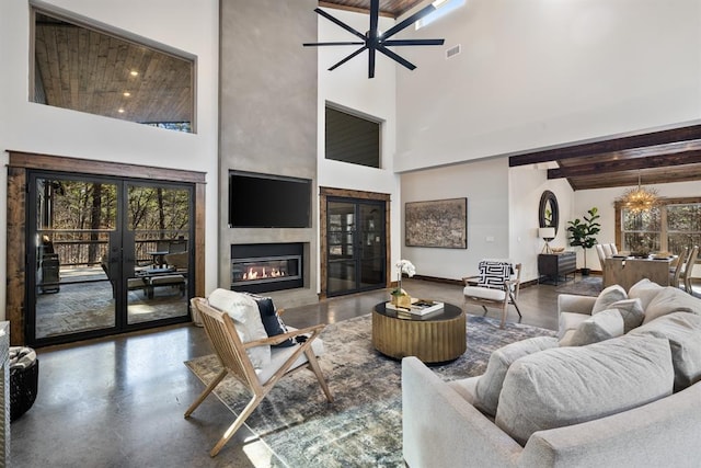 living room featuring french doors, concrete flooring, beam ceiling, ceiling fan with notable chandelier, and a high ceiling