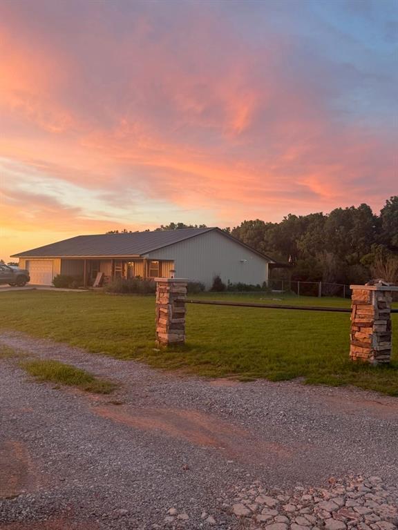 728 S Carol St, Carnegie, OK 73015 - property exterior at dusk with gravel driveway, an attached garage, and a lawn