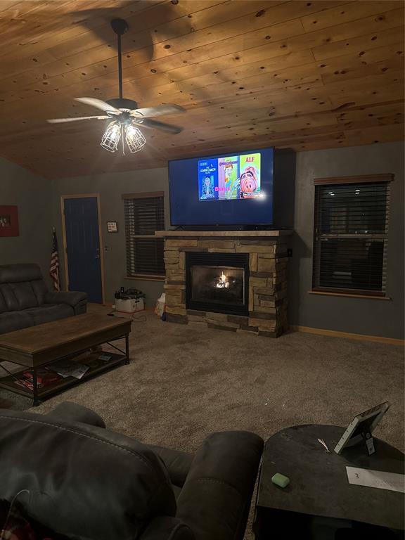728 S Carol St, Carnegie, OK 73015 - living area with ceiling fan, carpet flooring, vaulted ceiling, a stone fireplace, and wooden ceiling