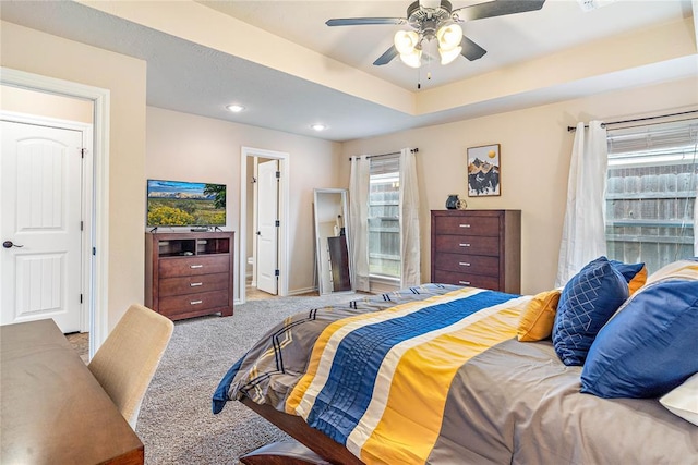 carpeted bedroom with ceiling fan and a tray ceiling