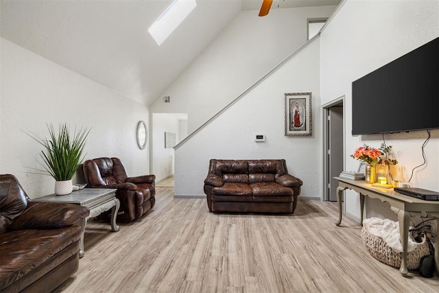 living room featuring ceiling fan, a skylight, high vaulted ceiling, and light hardwood / wood-style flooring