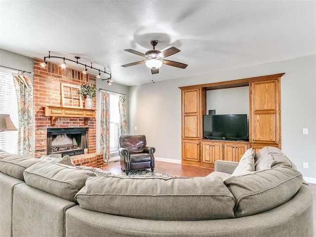 living room with rail lighting, a textured ceiling, a brick fireplace, light hardwood / wood-style flooring, and ceiling fan