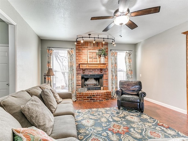 living room featuring ceiling fan, wood finished floors, plenty of natural light, and a brick fireplace