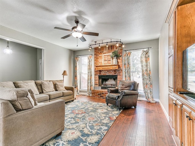 living room featuring ceiling fan, a fireplace, rail lighting, a textured ceiling, and hardwood / wood-style floors