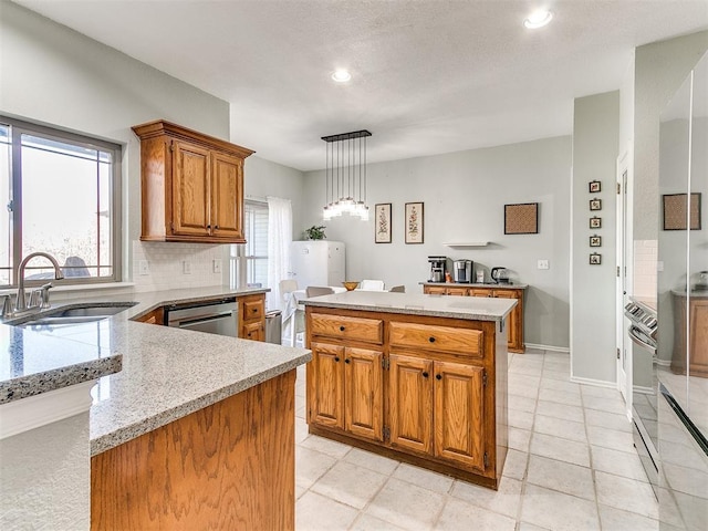 kitchen with brown cabinetry, stainless steel dishwasher, a sink, and a wealth of natural light