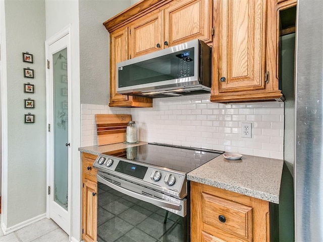 kitchen featuring stainless steel appliances, light tile patterned floors, backsplash, and light stone counters