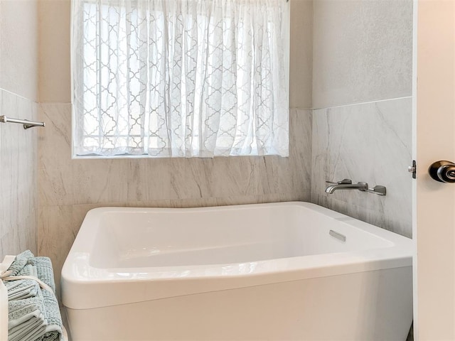bathroom featuring a bath, a healthy amount of sunlight, and tile walls