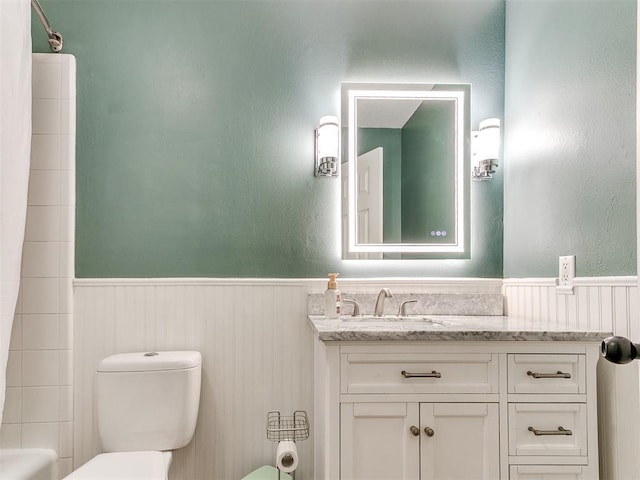 full bath with toilet, a wainscoted wall, and vanity