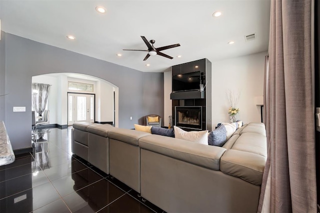 tiled living room with ceiling fan and a fireplace