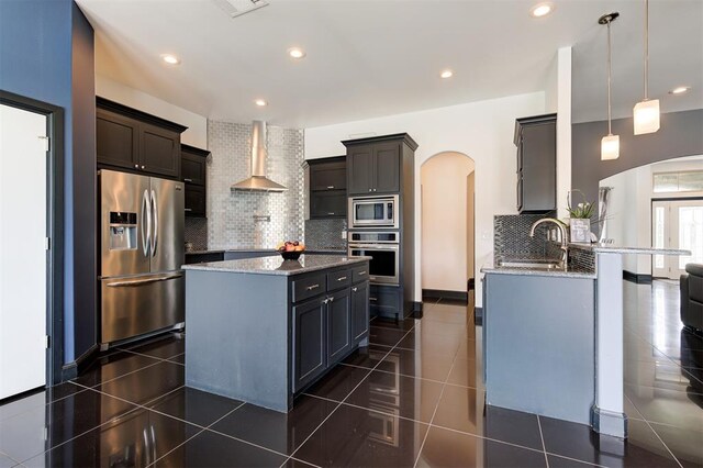 kitchen with sink, appliances with stainless steel finishes, a center island, decorative light fixtures, and wall chimney exhaust hood