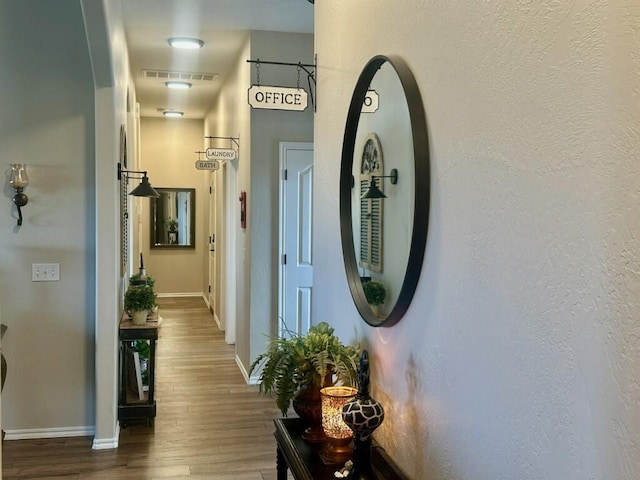 corridor featuring visible vents, baseboards, and wood finished floors